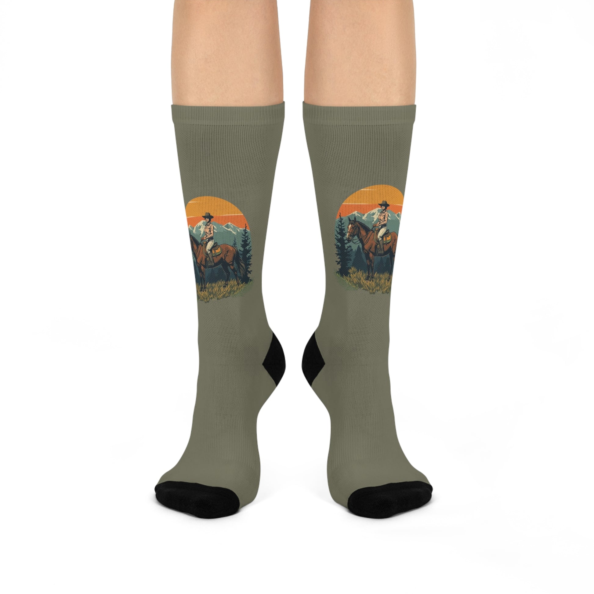 White cushioned crew socks with an olive sunset, pine trees, and a horse and rider design climbing the calf.