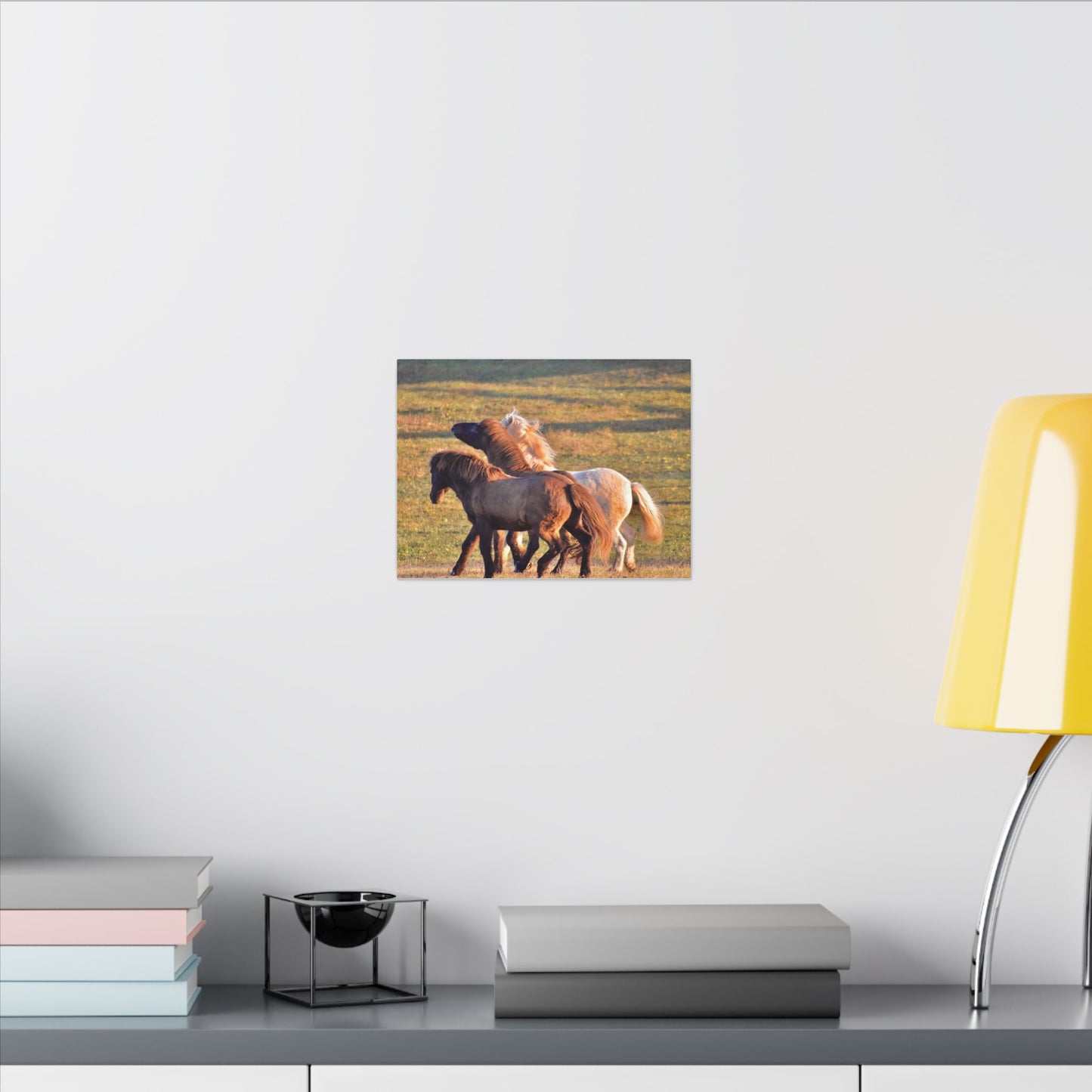 Canvas print of three horses on a grassy field hanging on a wall above a desk.