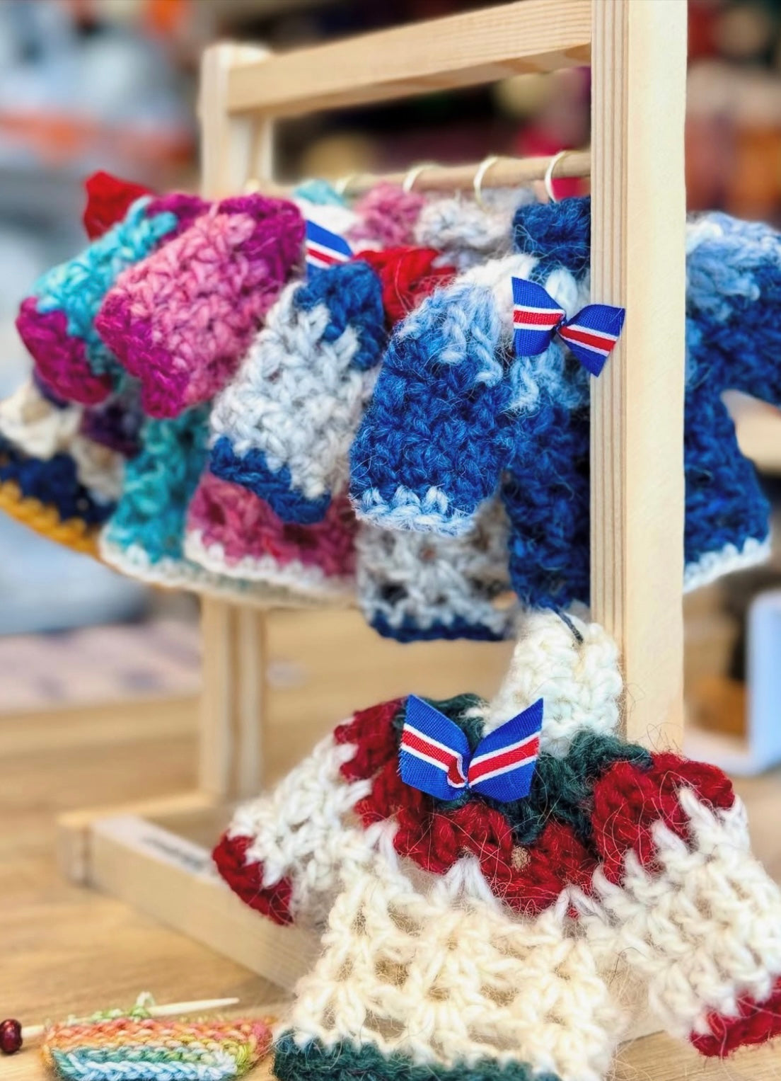 Colorful crocheted mini sweaters with bow ties on a wooden stand.